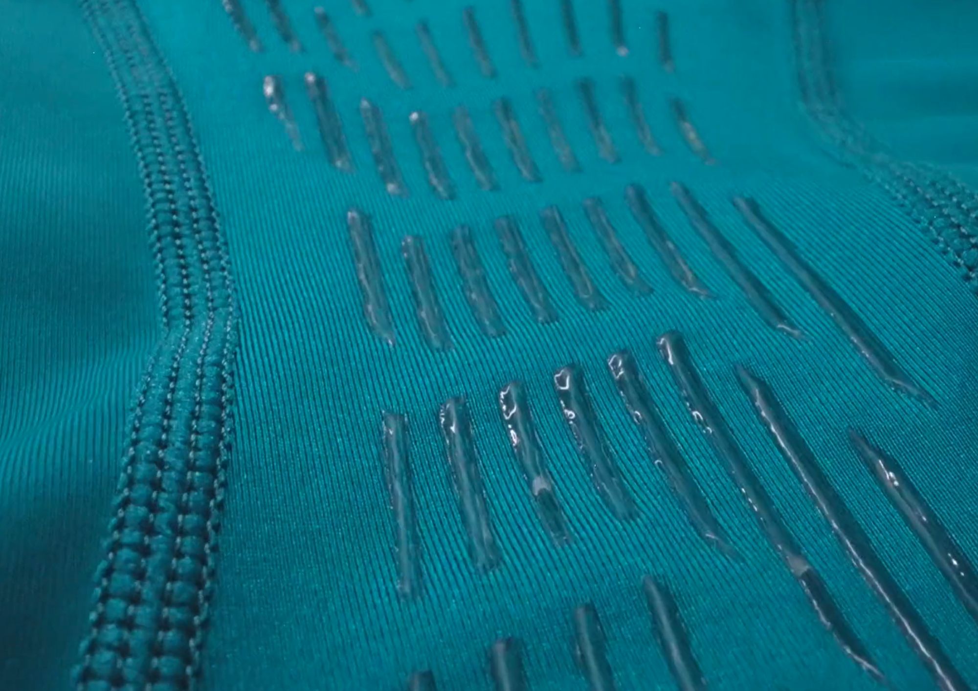 Close-up of textured teal fabric with metallic stitching details.