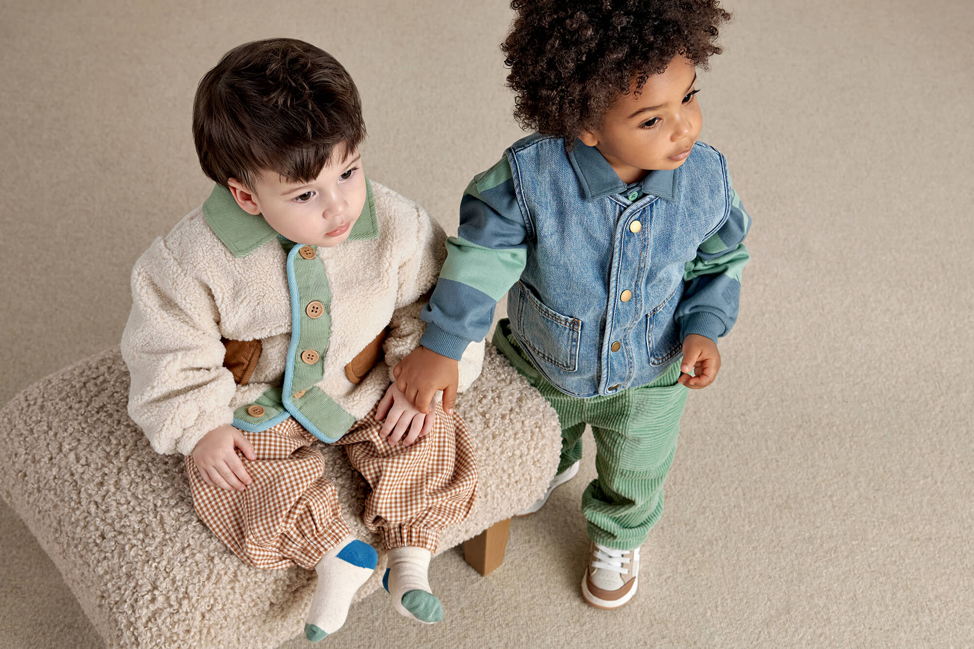 Two children sitting together on a chair, one holding the other's hand.