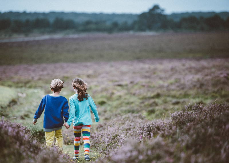 Two children, a girl and boy, marching hand in hand along a path through the heather. They look like they’re on an adventure