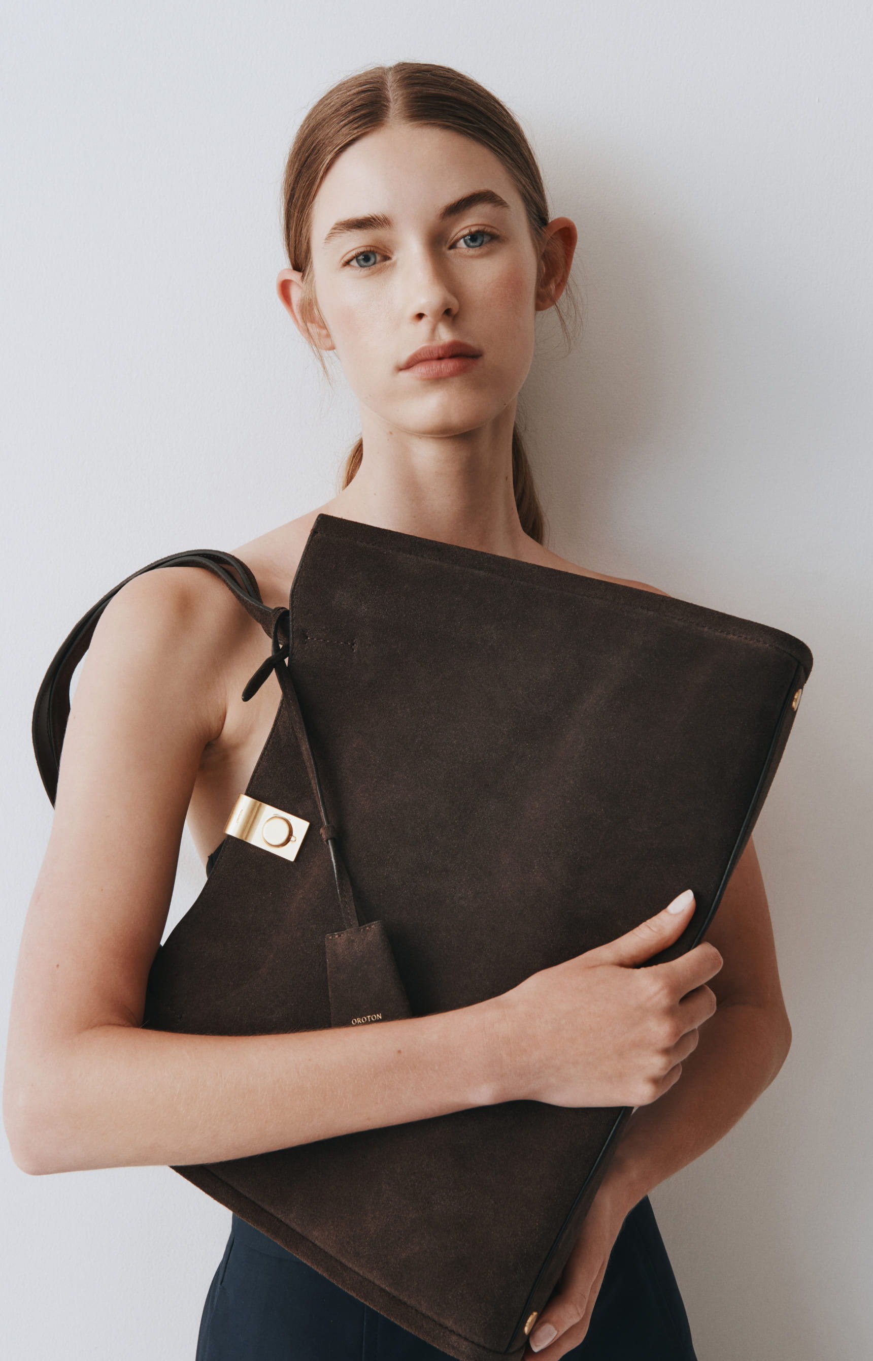 Model holding a large dark bag against a neutral background.