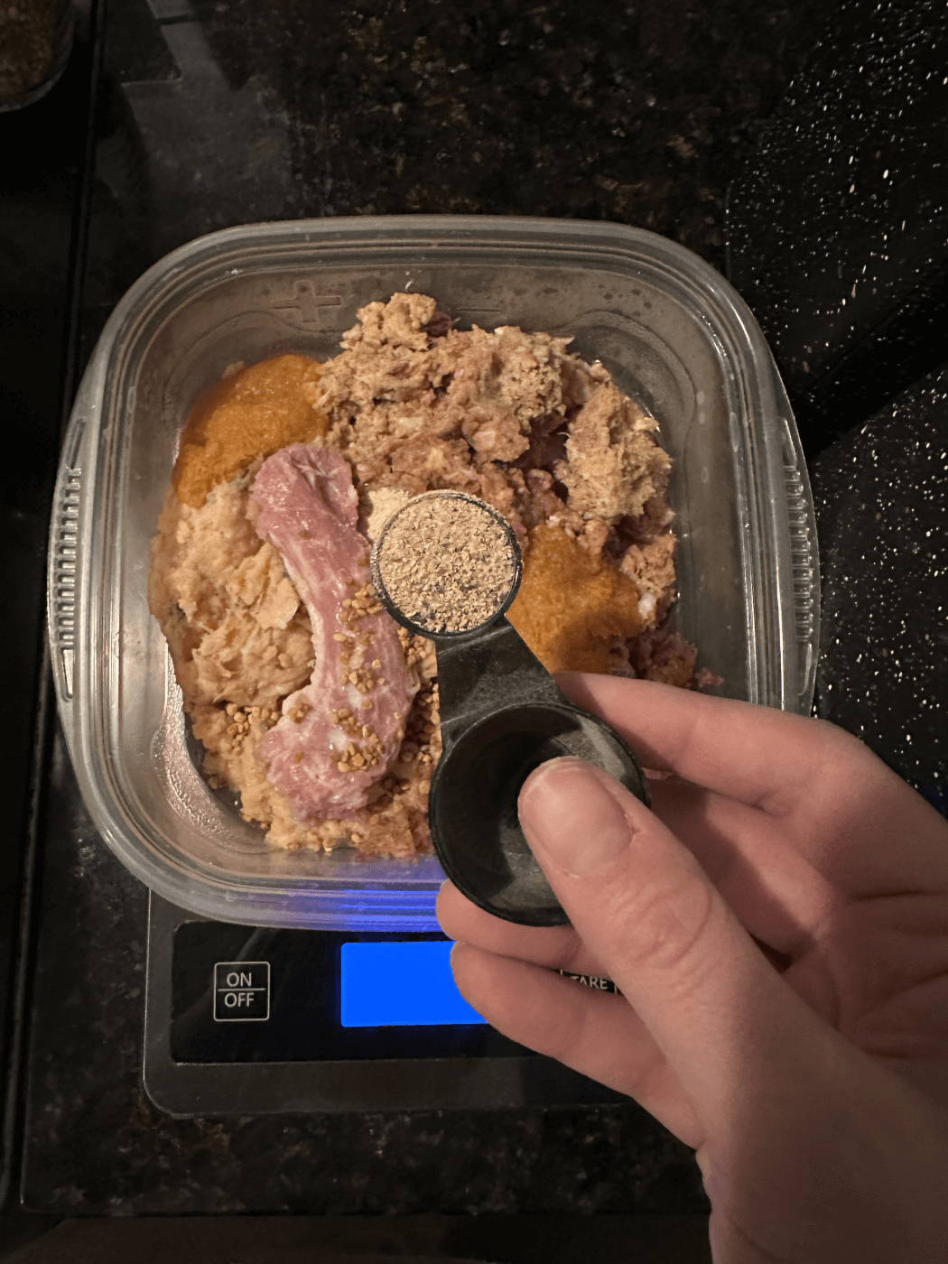 Hand of person adding supplement powder over raw meat in Tupperware.