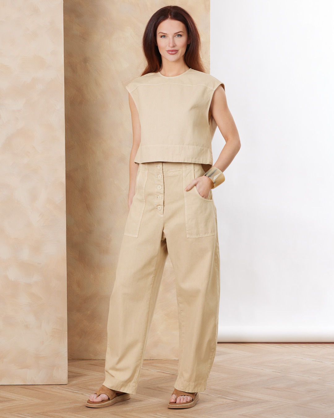 A woman in beige clothing stands against a neutral background.