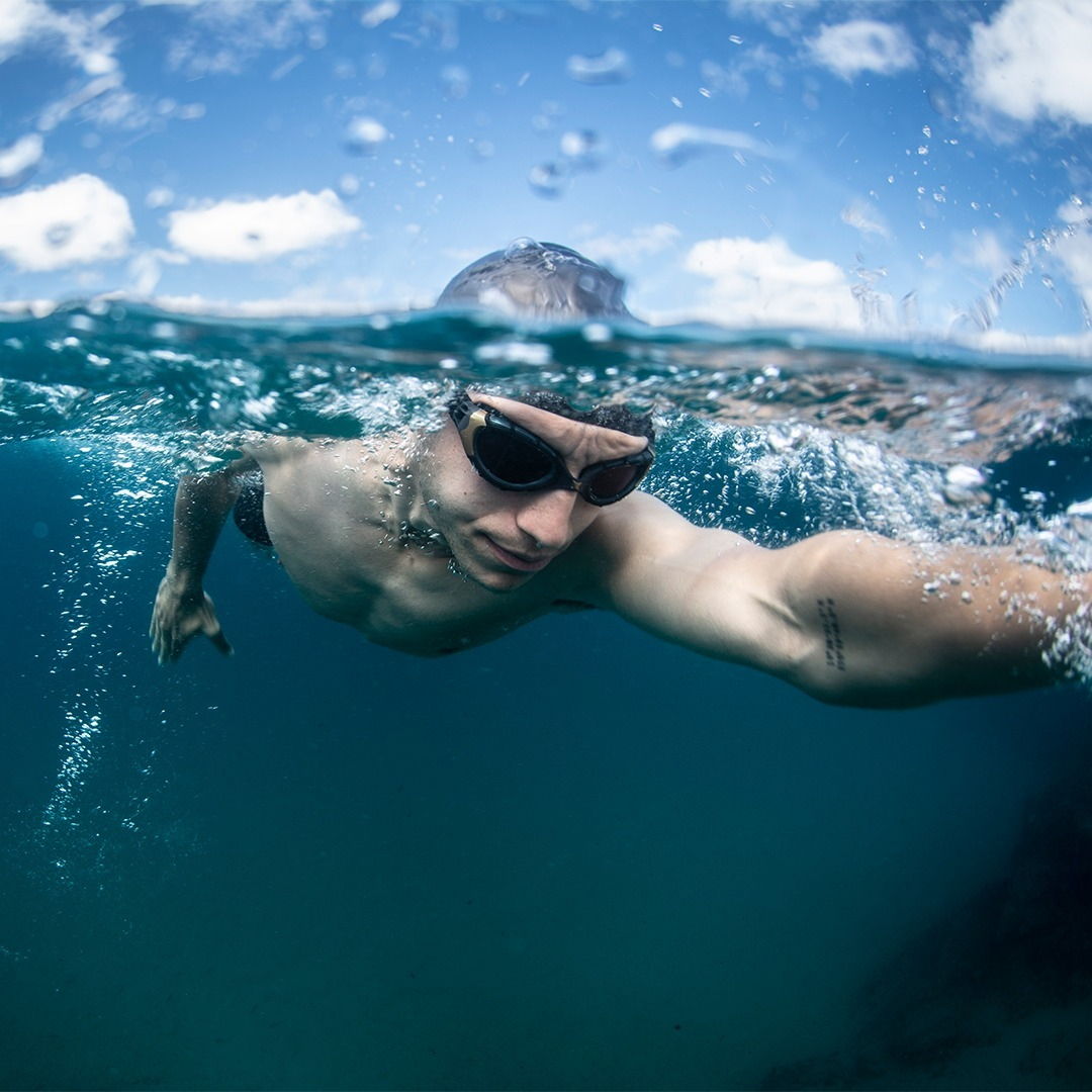 Ein Triathlet beim Schwimmen mit einer Schwimmbrille von unten aus dem Wasser fotografiert.