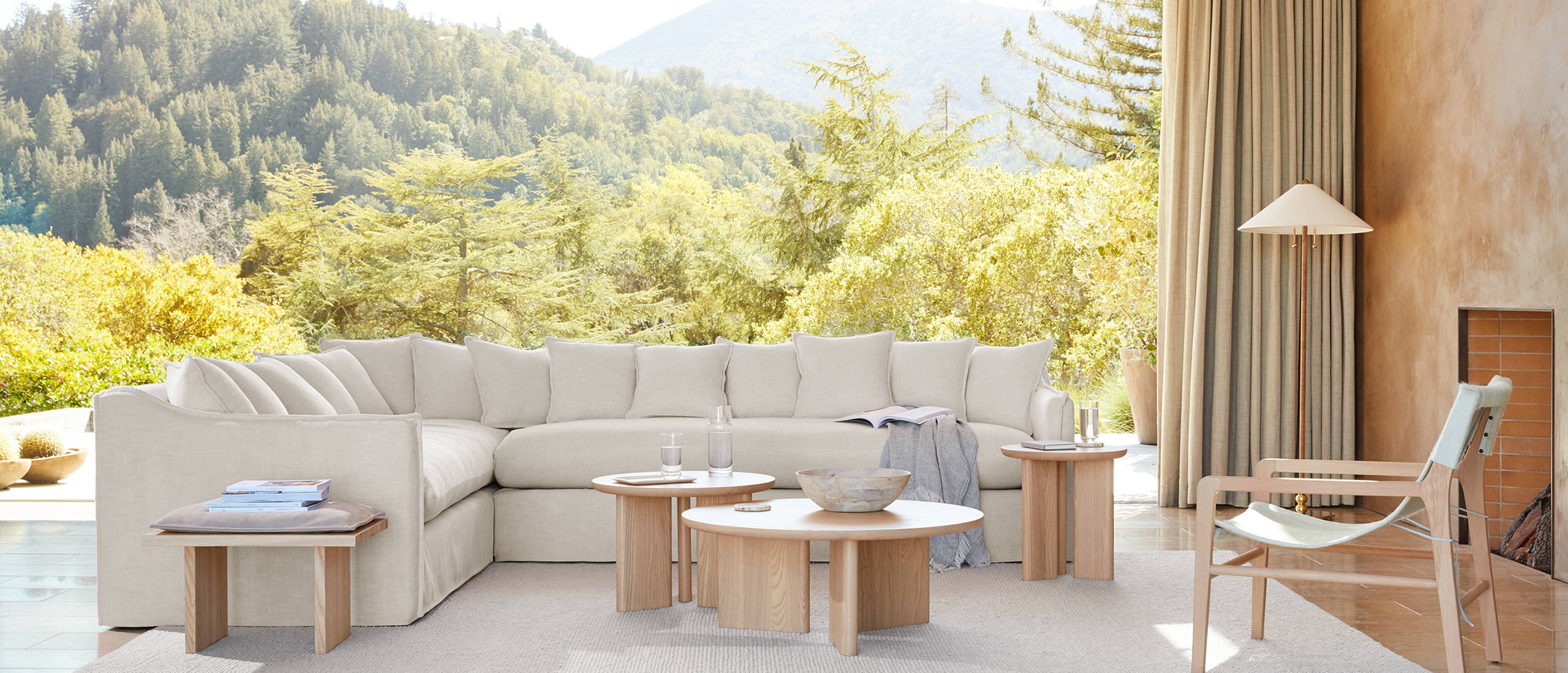 A living room furnished with a Reyes Stool and Morro Tables in a Natural Ash finish, a Hayes Chair in beech and Snow hair-on-hide, and a Dune sectional in Buff performance chenille.