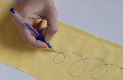 image of a blue heat erasable fabric marking pen being tested on a piece of yellow fabric