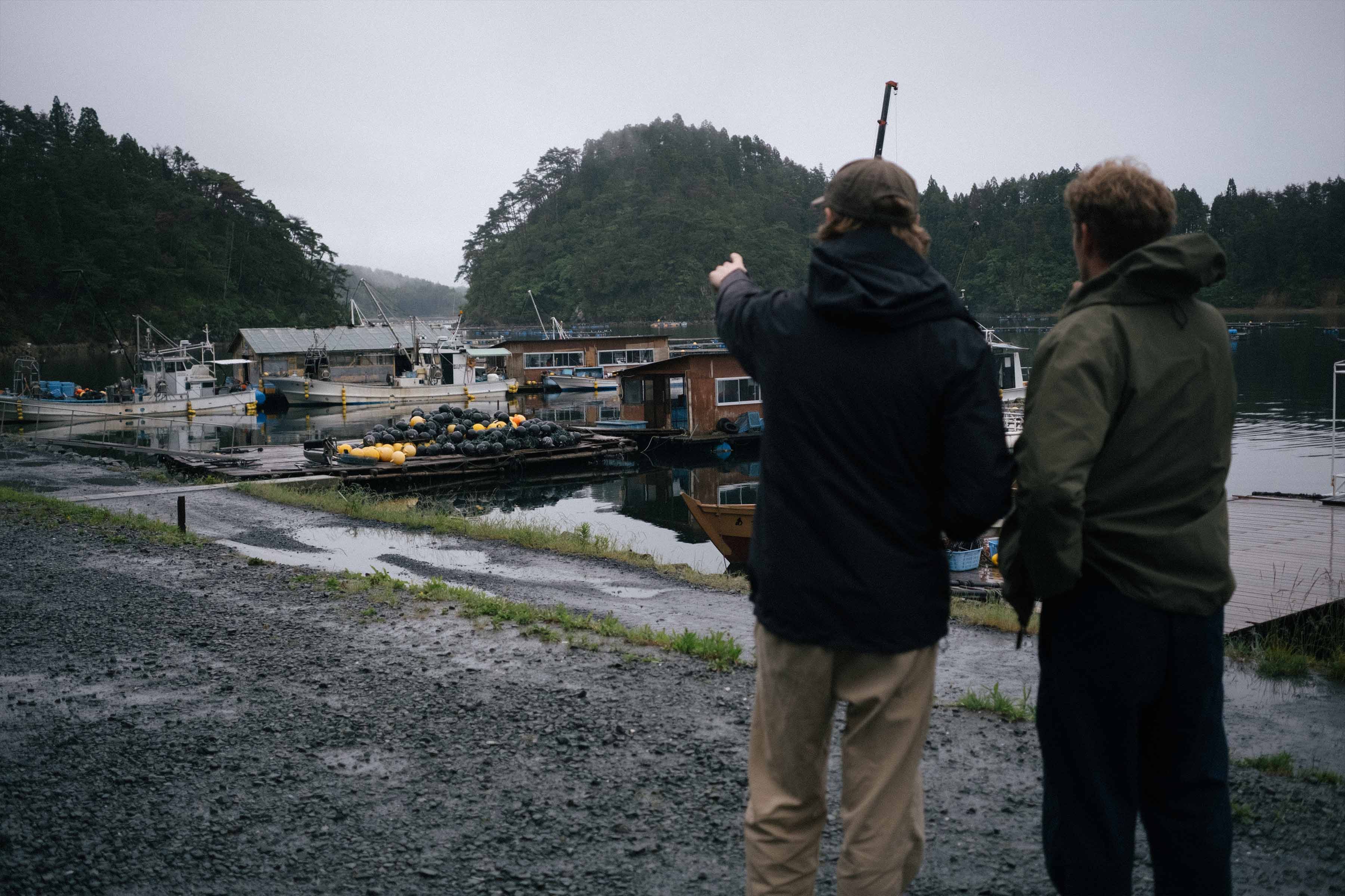 Two people observing boats at a dock on a rainy day.