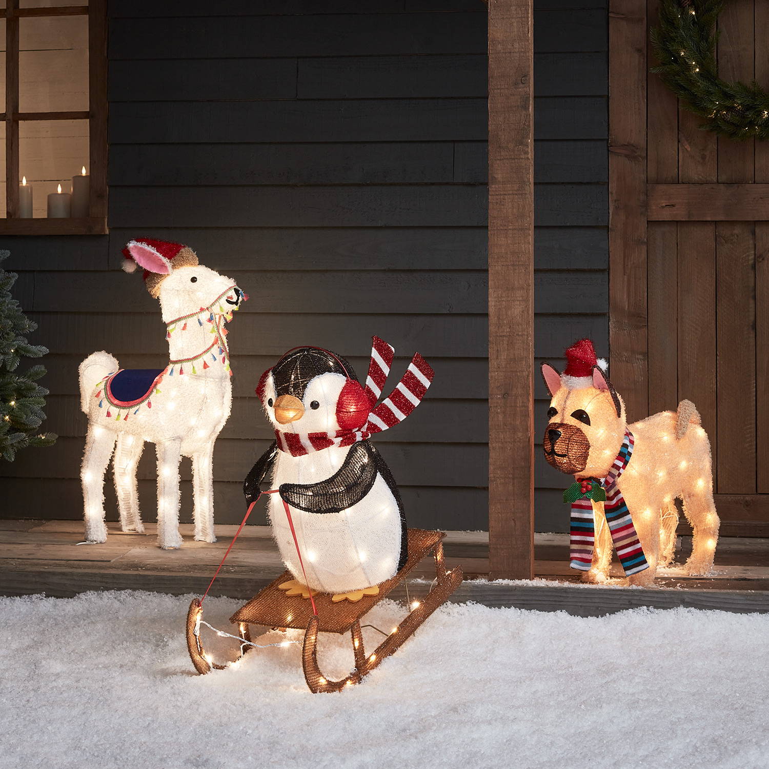 3 light up Christmas figures in a snowy porch setting outdoors.