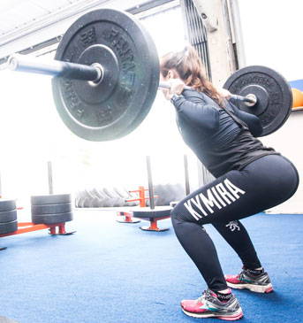 A woman in KYMIRA gear in mid-squat with a barbell across her shoulders.