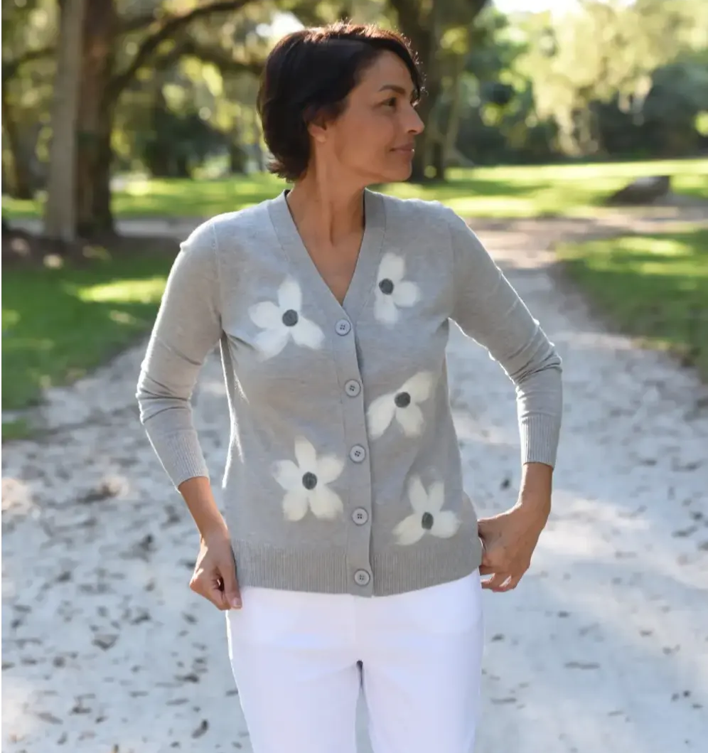 A woman with short, dark hair and a floral sweater looks to the side as she stands on a footpath in the woods. 