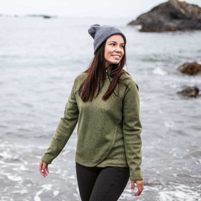 Woman wearing green Harlow Zip Neck Fleece walking along shore in fall.