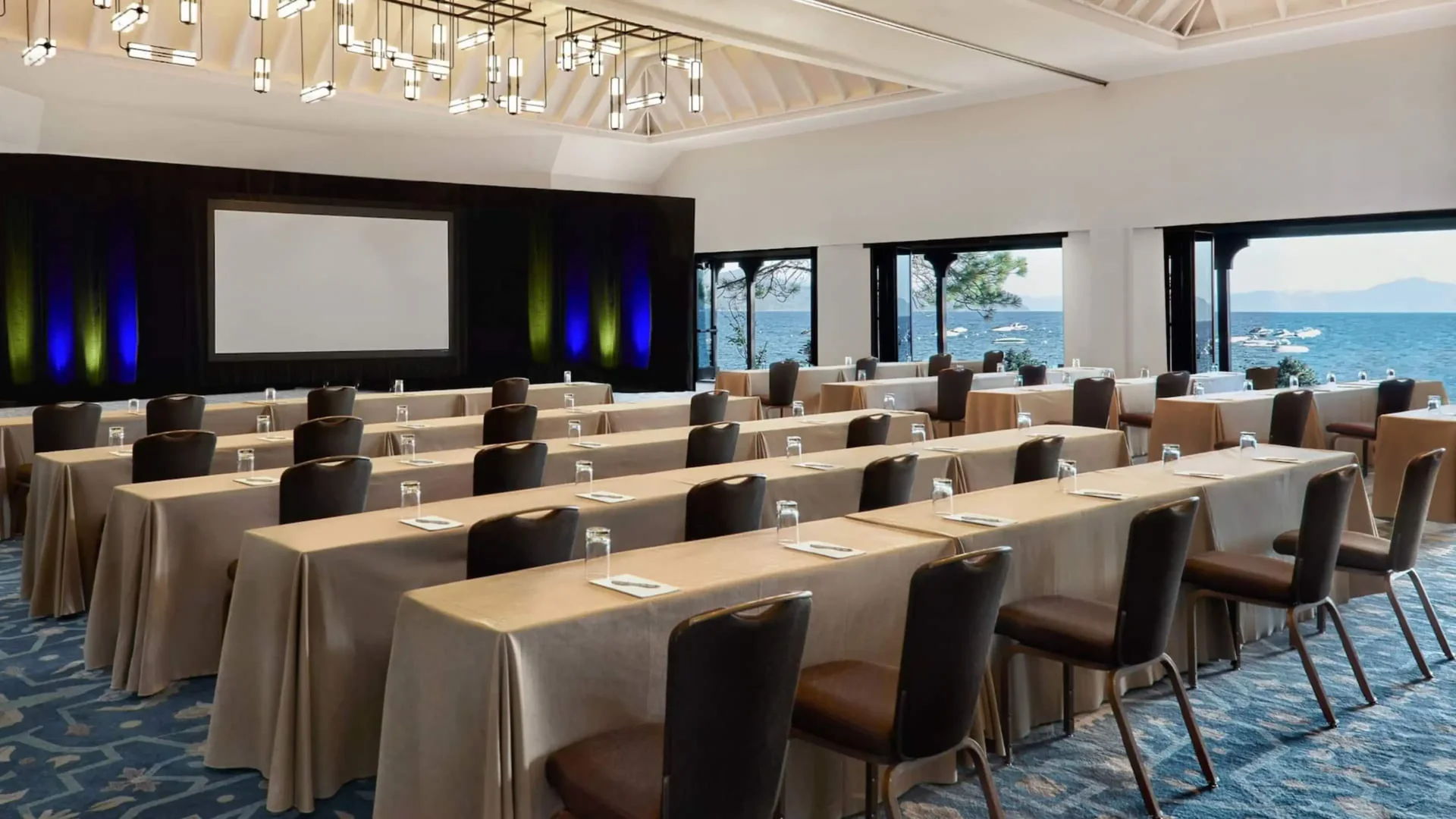 Conference room setup with tables, chairs, and a projector screen by the ocean.