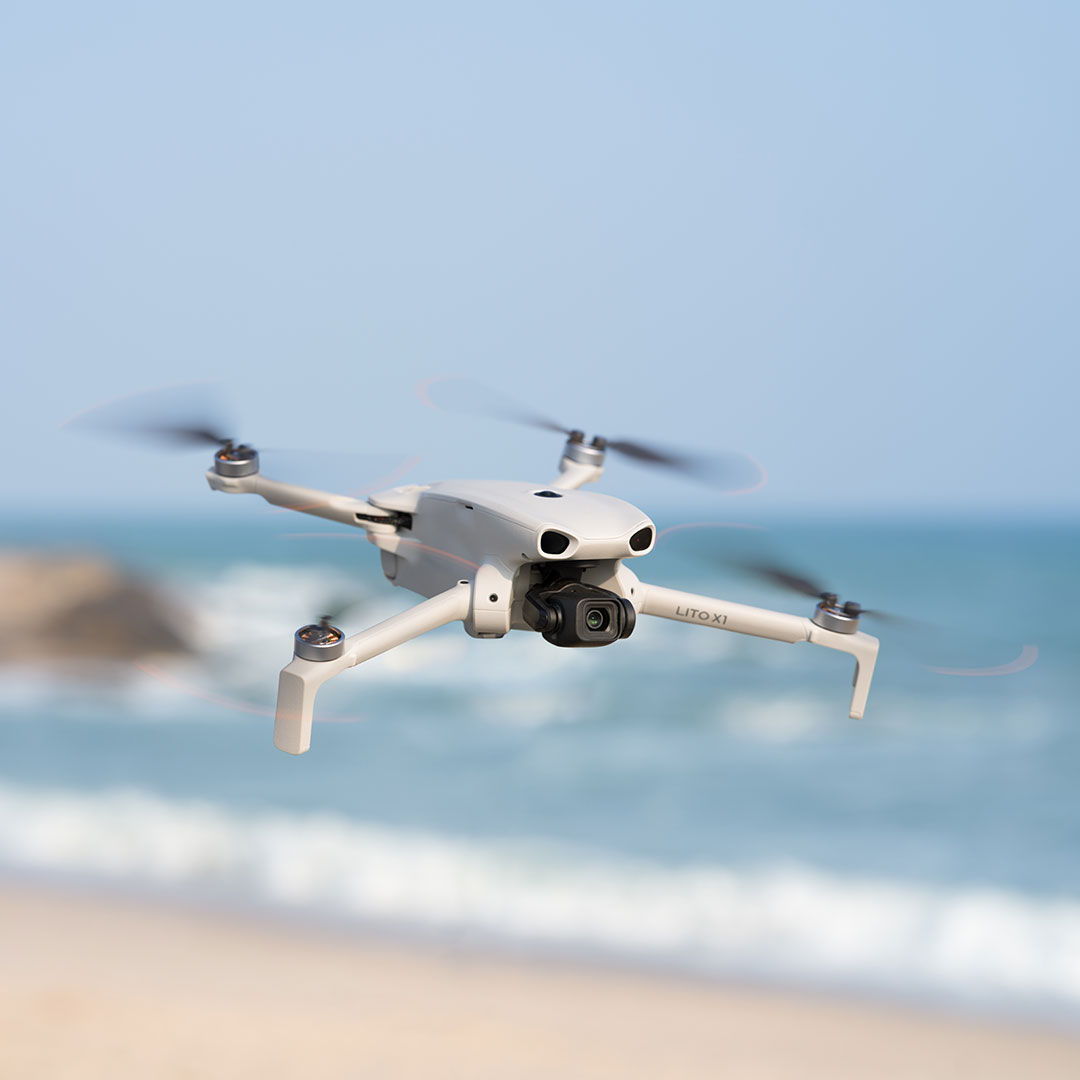 A DJI Lito X1 drone flying near a beach with ocean waves in the background.