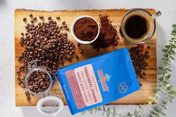 Coffee beans, ground coffee, cup, and a blue coffee bag on a wooden surface.