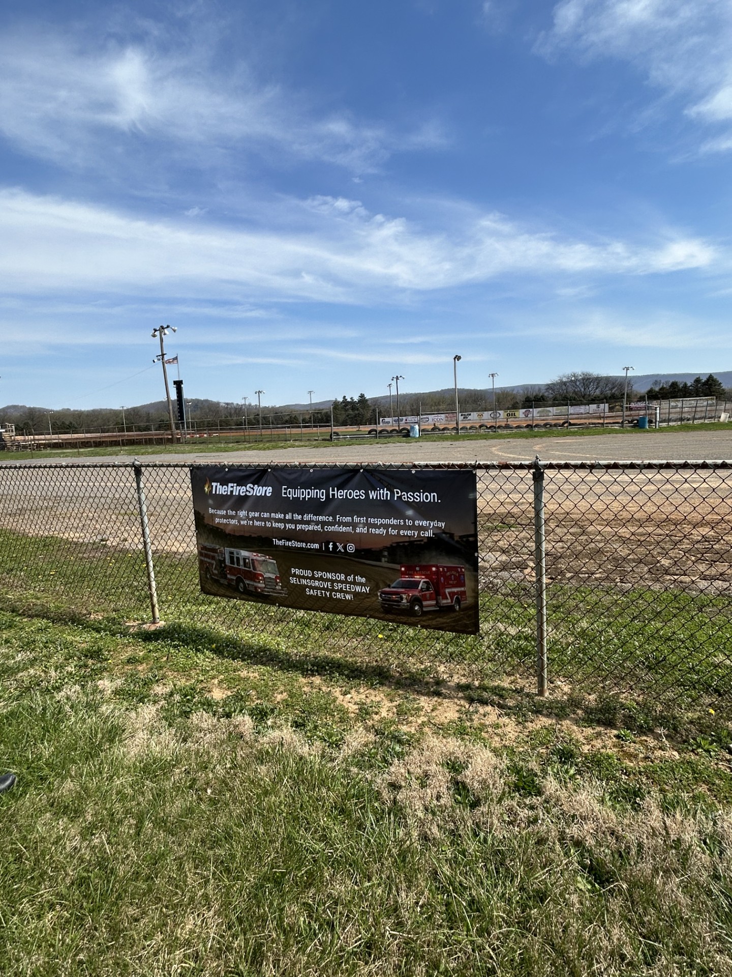 Banner advertisement on a fence near a baseball field under a blue sky.