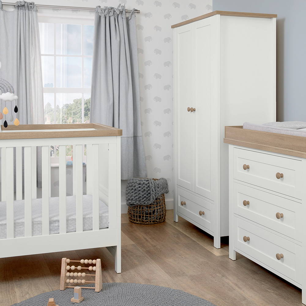 A white nursery furniture set featuring a wardrobe, cotbed and dresser changer sits in a grey nursery.