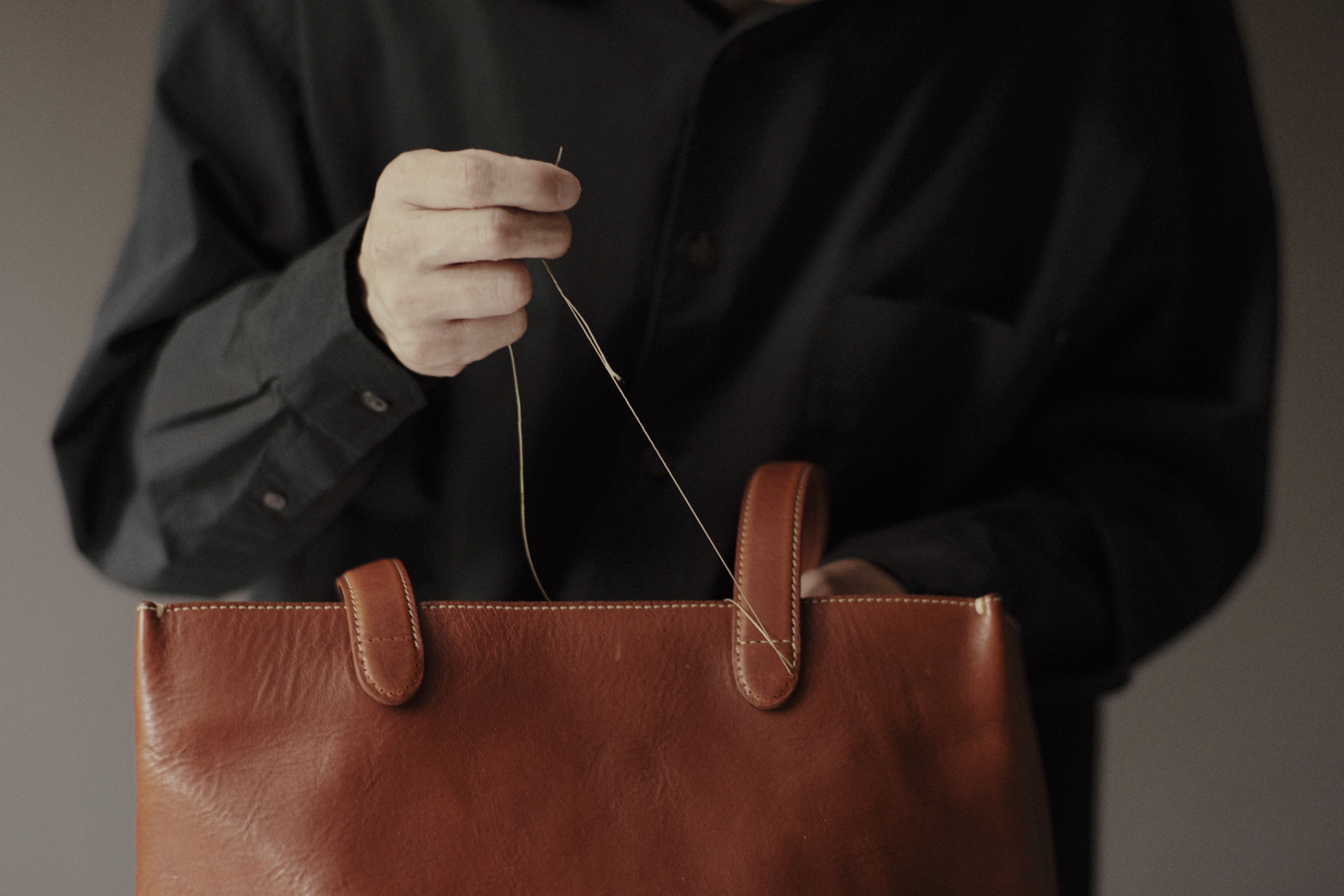 Person holding a brown leather bag with a black shirt.