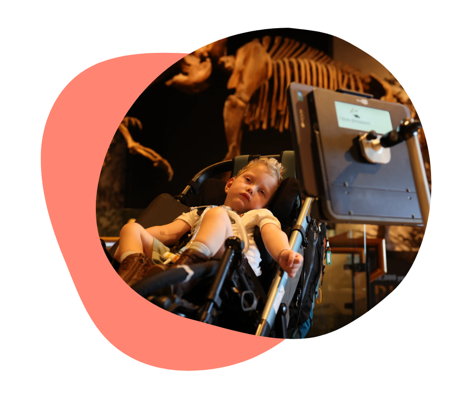 Child in a wheelchair with Grid Pad in front of a dinosaur display. 