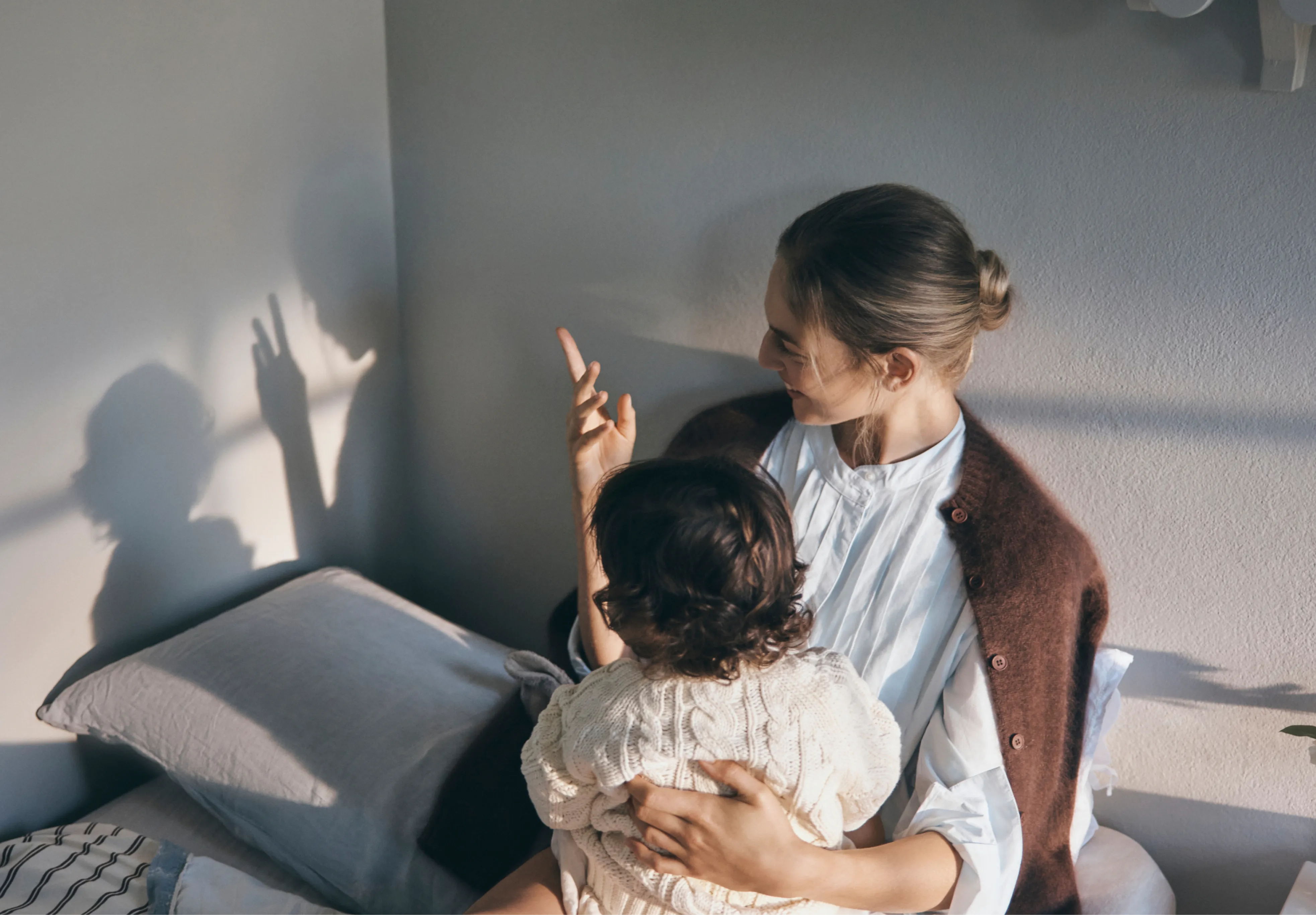 A mother and child sitting together, casting playful shadows on the wall.