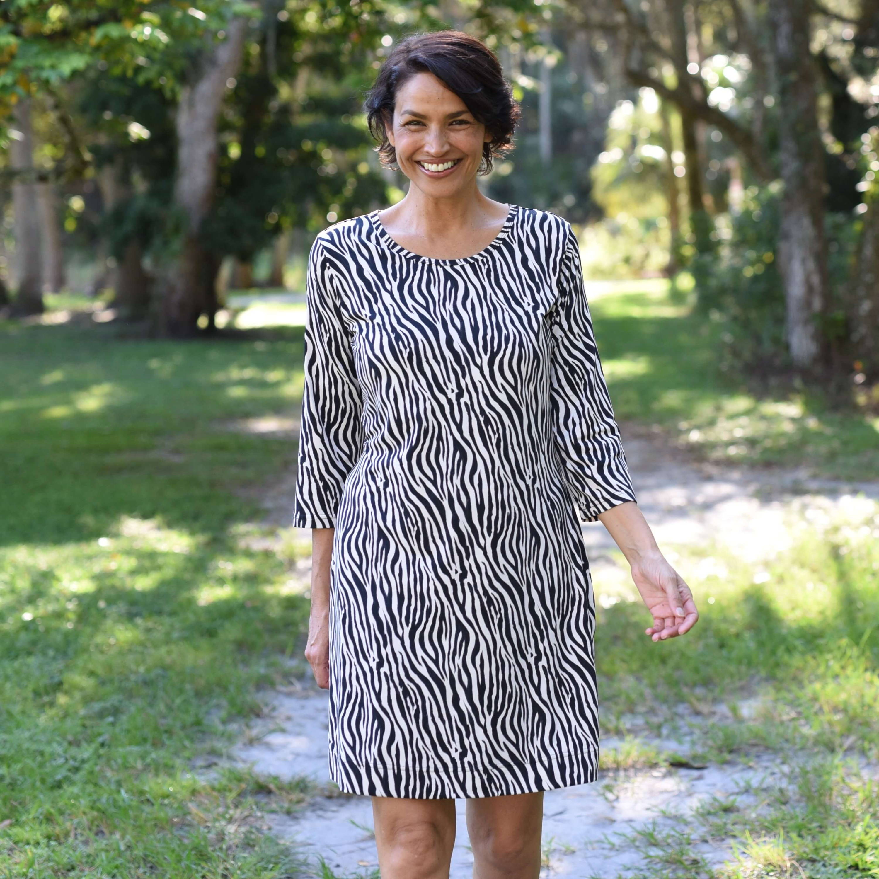 A smiling woman with short, dark hair walks down a footpath in a park. 