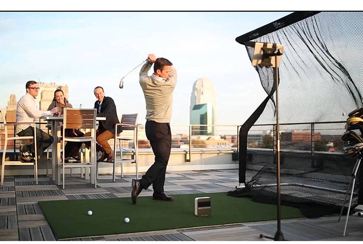 A man using the SkyTrak on a rooftop simulator with friends