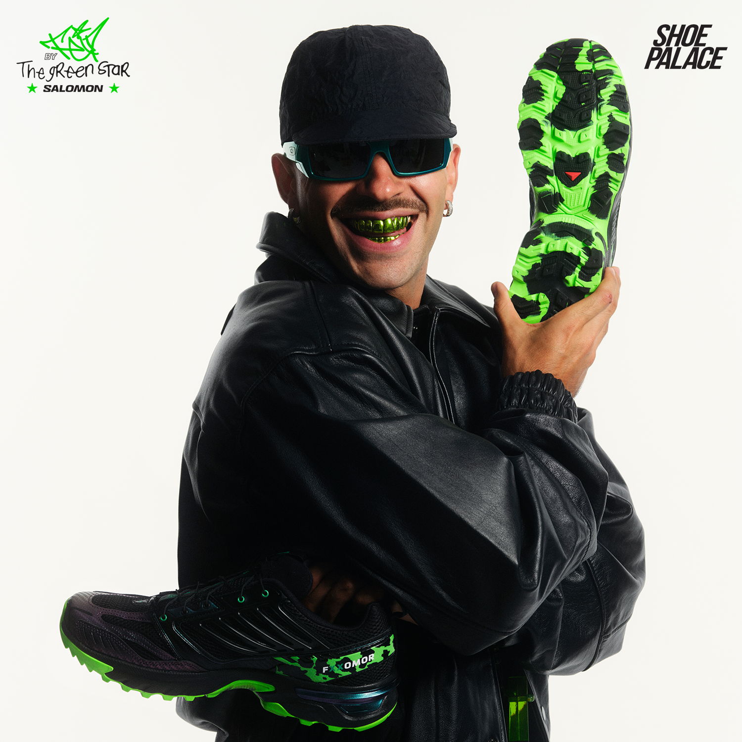Person in black clothing holding a green sneaker, smiling with sunglasses.