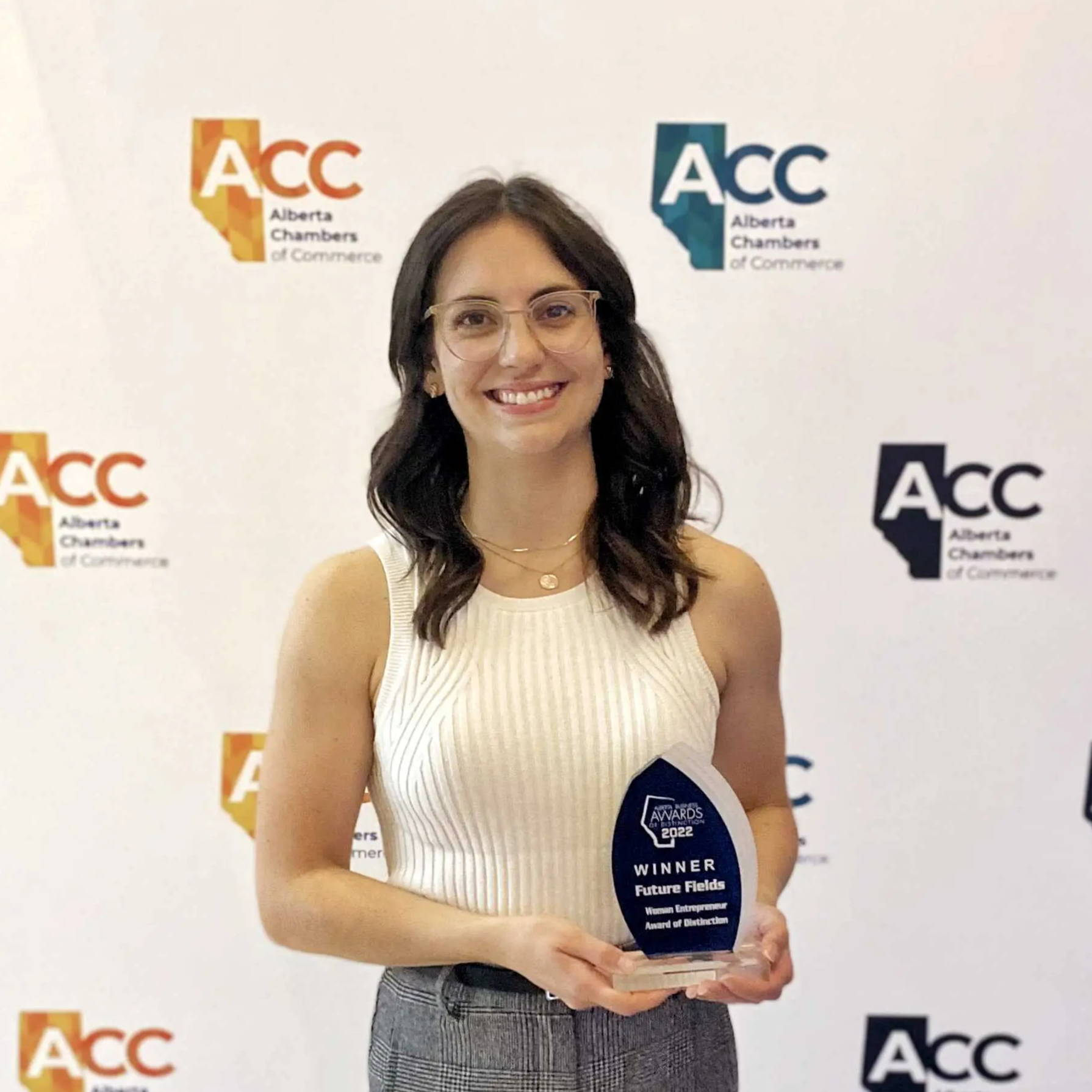 Jalene Anderson-Baron wins Alberta Woman Entrepreneur Award of Distinction for 2022.  Jalene stands in front of an ACC backdrop holding an award.
