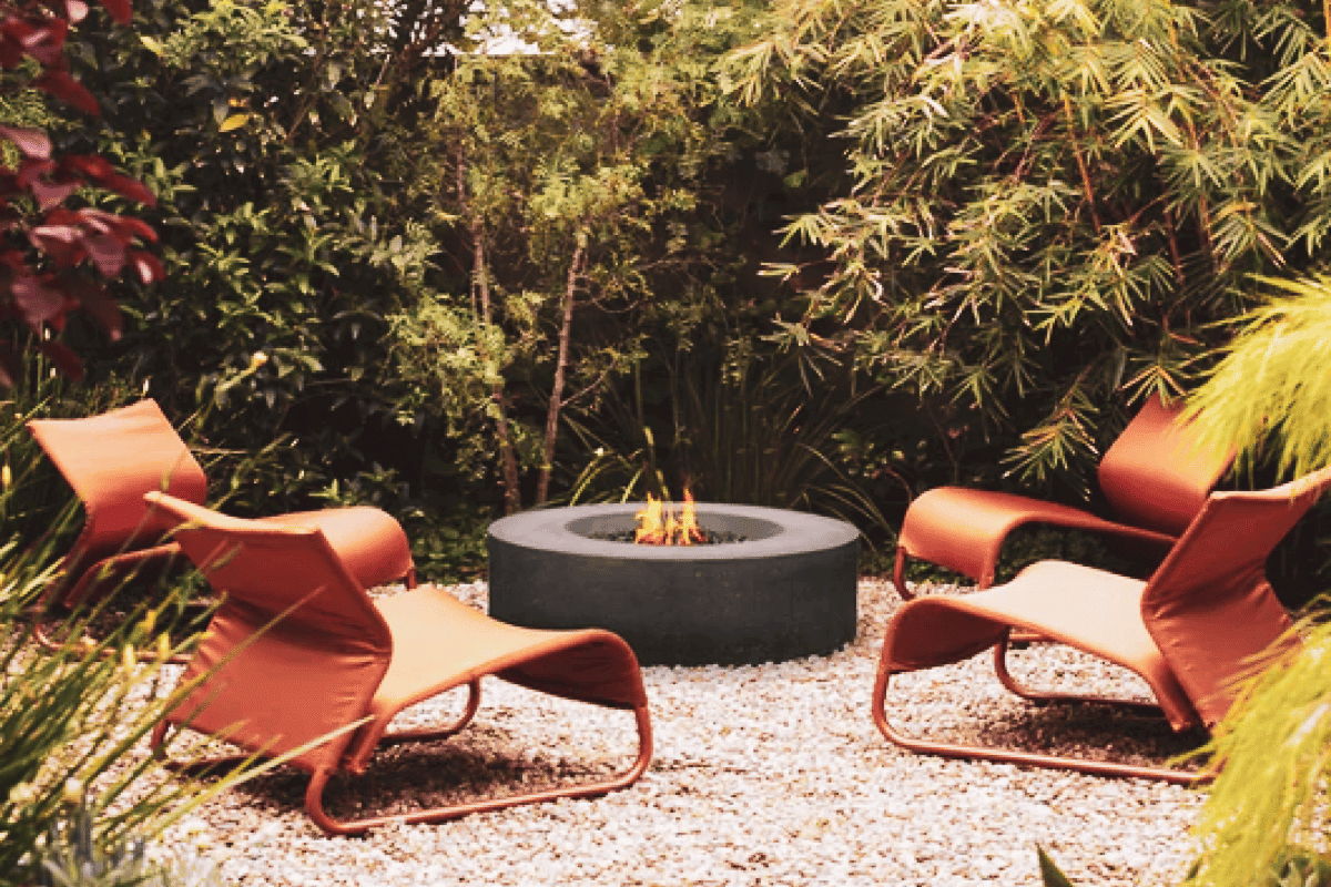 Round outdoor fire pit with orange lounge chairs arranged for a cozy garden seating area.