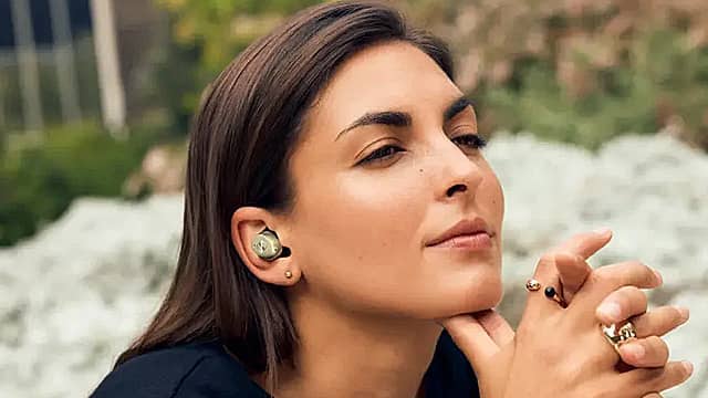 Woman wearing earbuds, eyes closed, in a serene outdoor setting.