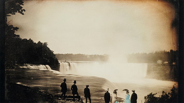 Silhouettes of people near a waterfall in a vintage photograph.