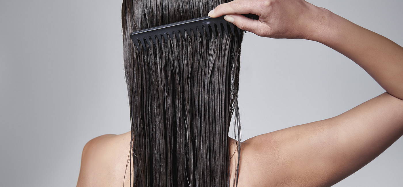 Back view of a person with wet, straight hair being combed with a black wide-tooth comb.