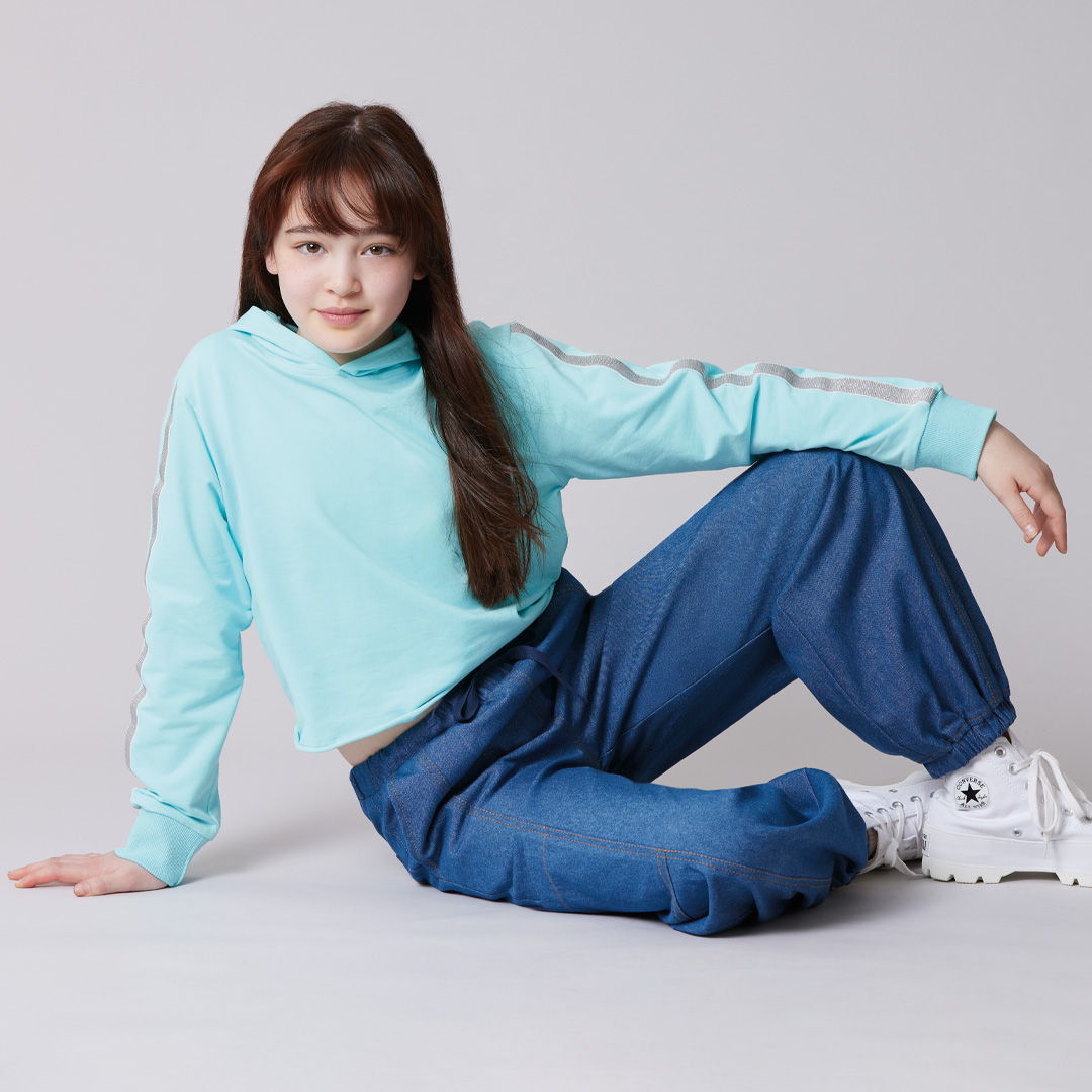 A person in a light blue top and blue pants sits on the floor.