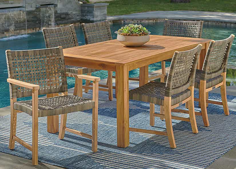 Wooden dining table with wicker chairs beside a pool.