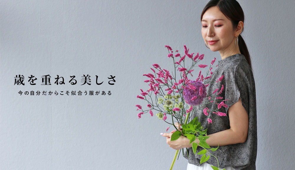Woman holding colorful flowers against a neutral background, showcasing beauty and elegance.