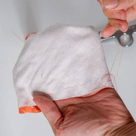 A hand holding a fabric tube with orange thread sewn all around
