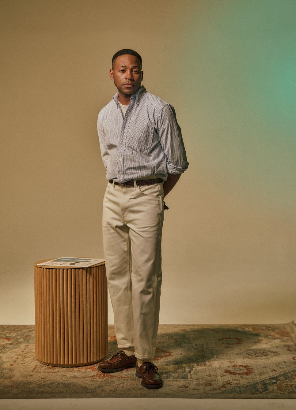A person standing beside a wooden table against a neutral background.