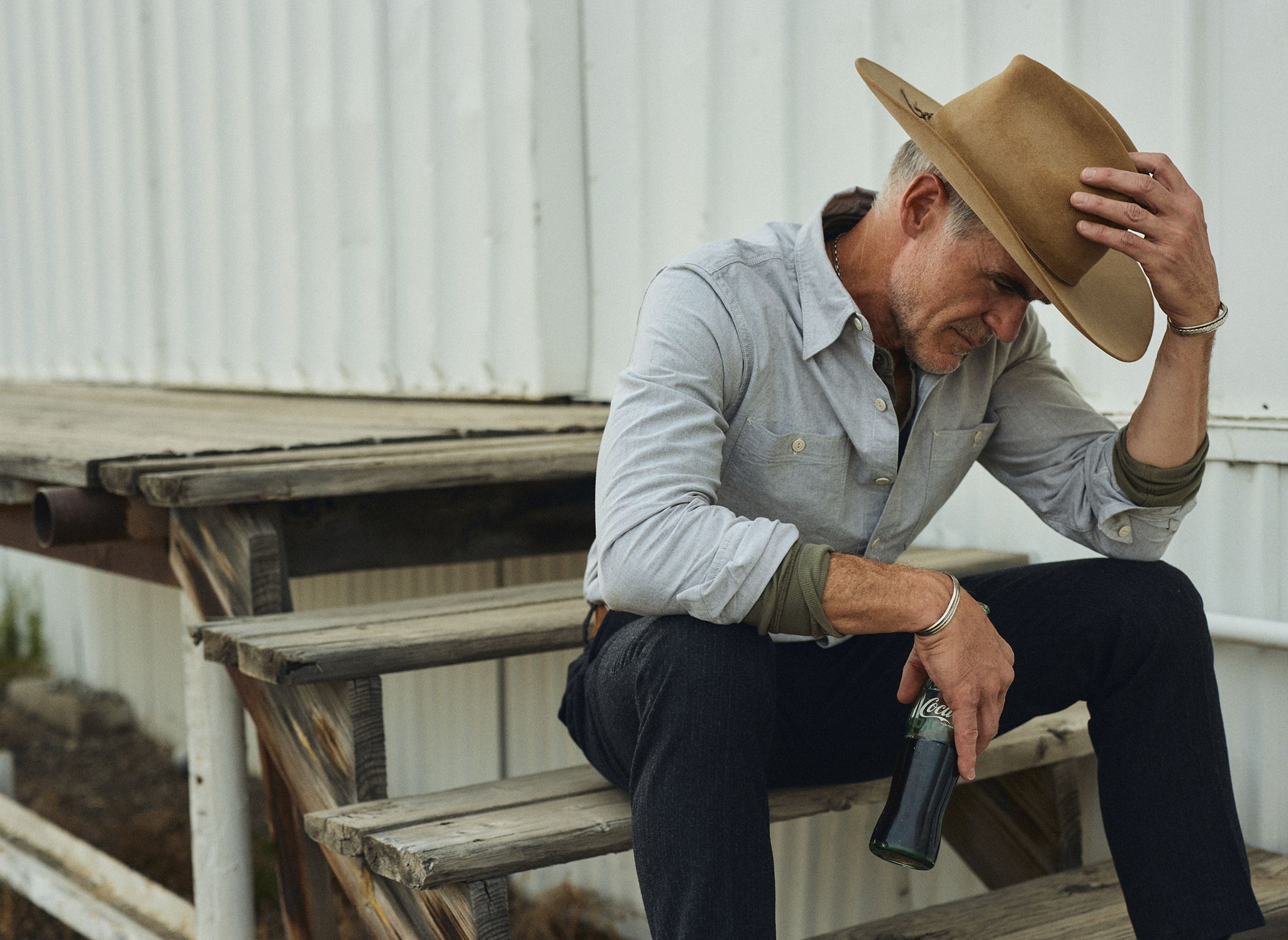 Micahel Kelly at an abadoned service station in Livingston, Montana drinking a Coke wearing Bridges Oxford Workshirt in Olive and the Rivay Italian Wool Suit in Charcoal Herringbone Trousers