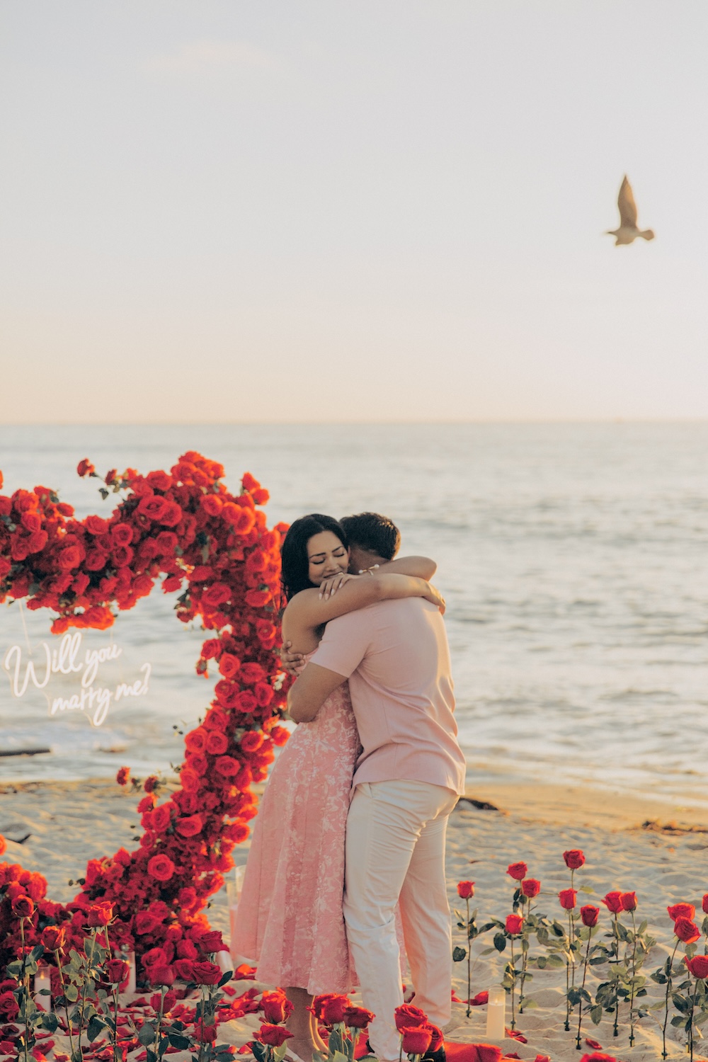 beachfront proposal in front of a floral heart