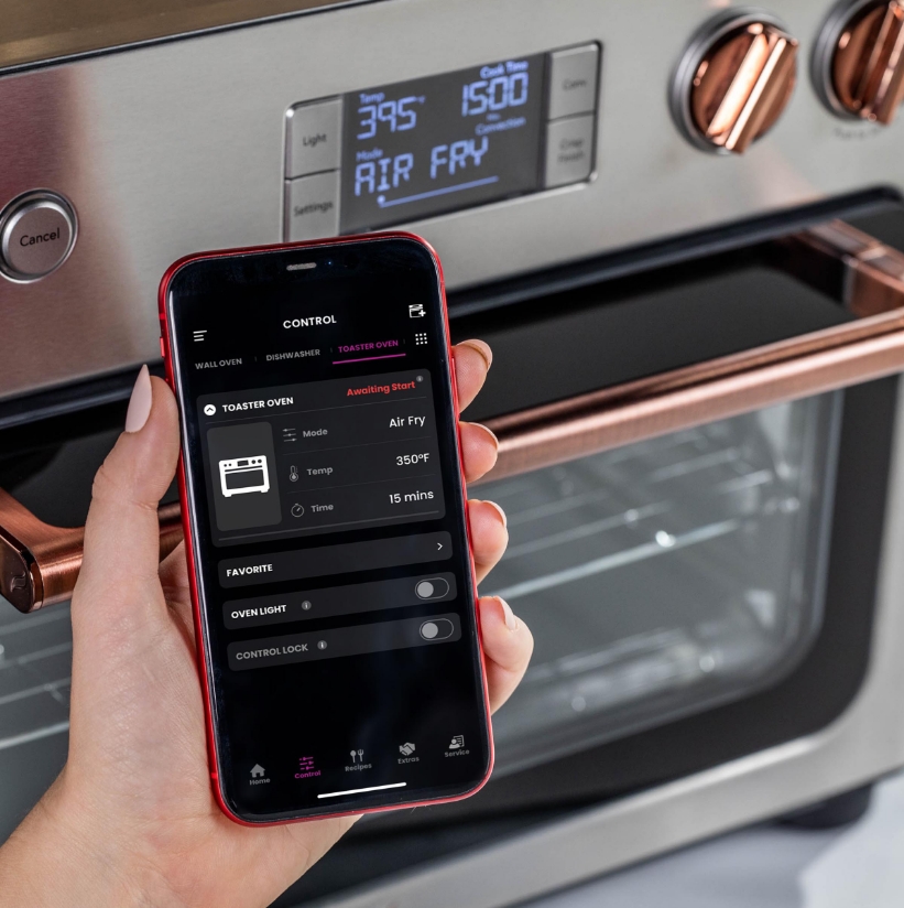 A hand holding a smartphone near a Cafe couture oven with digital display.