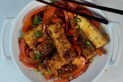 A bowl of stir-fried vegetables and spring rolls with chopsticks.