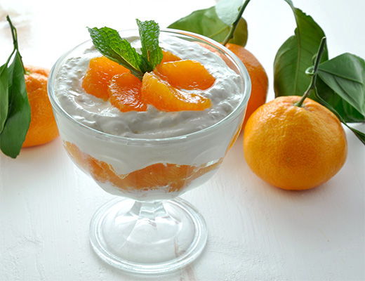 A dessert with cream, mandarin oranges, and mint leaves in a glass dish.