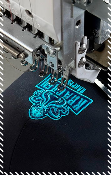 Industrial embroidery machine stitching a bright turquoise logo onto black fabric using satin stitch technique