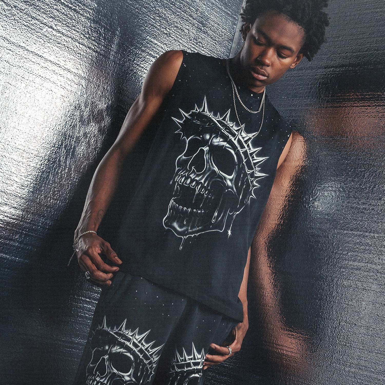 Person wearing black outfit with skull design, standing against reflective background.
