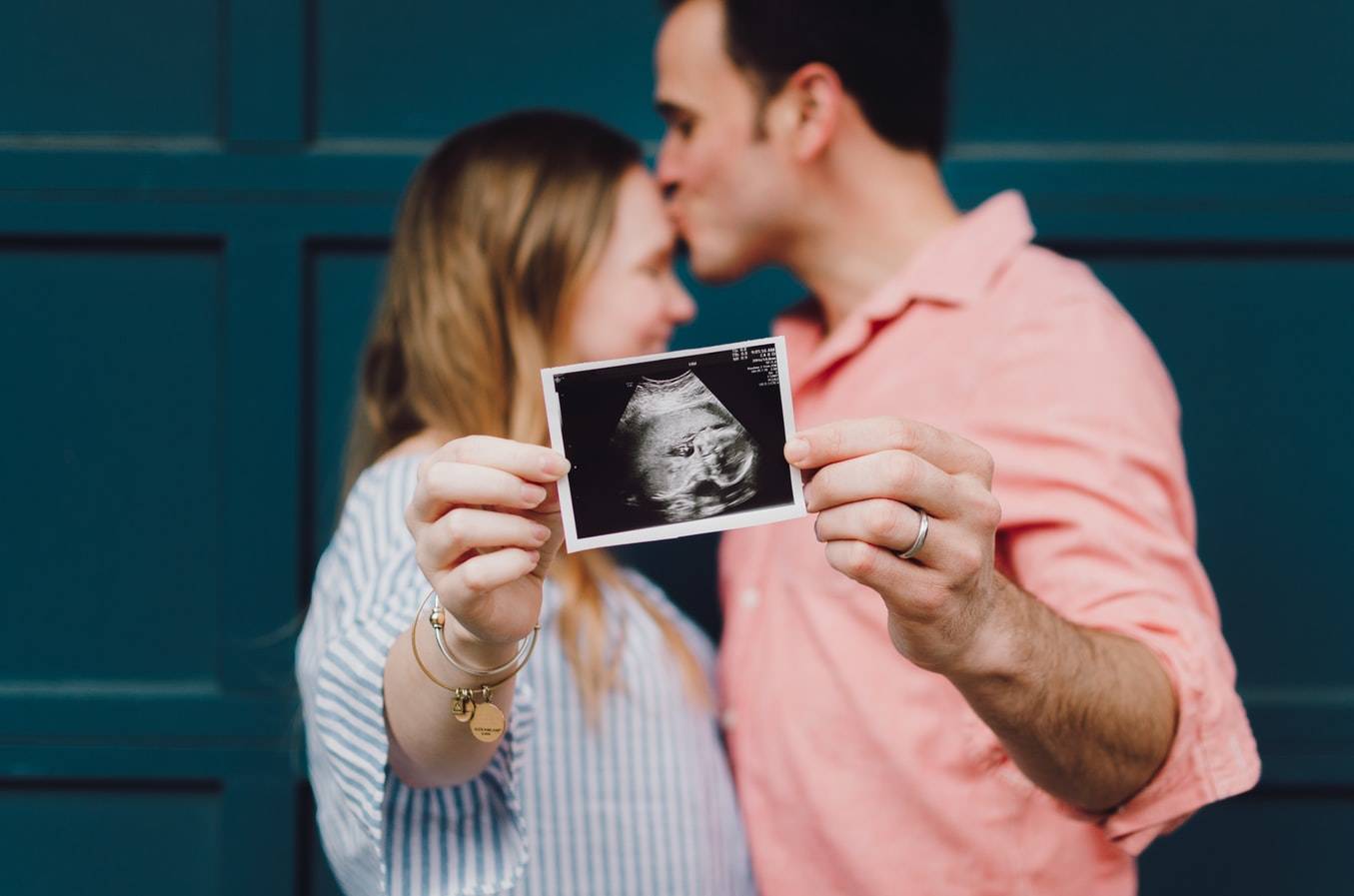 Man Kissing Woman's Forehead Whilst Holding Ultrasound Photo