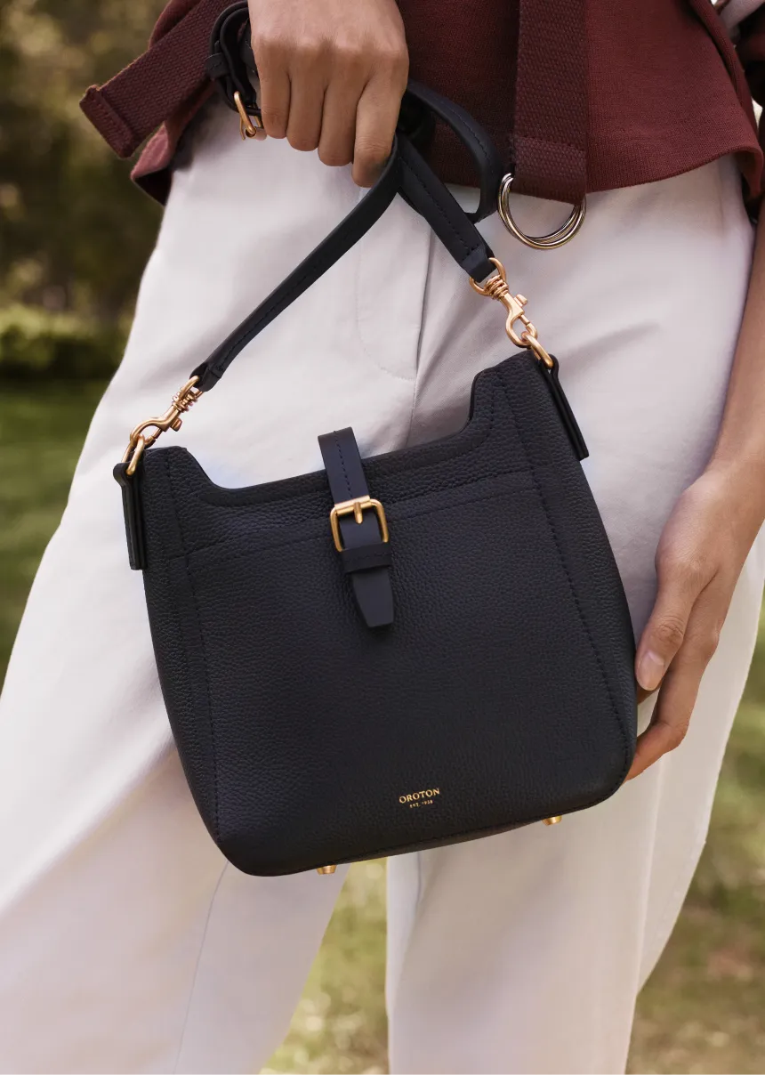 A person holding a stylish black handbag with a gold buckle.