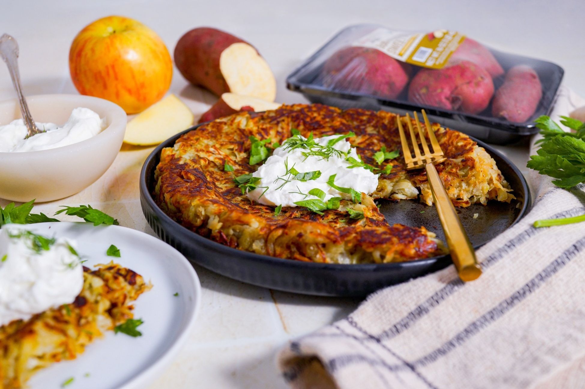 A dish of potato pancakes with yogurt, apples, and sweet potatoes on a table.