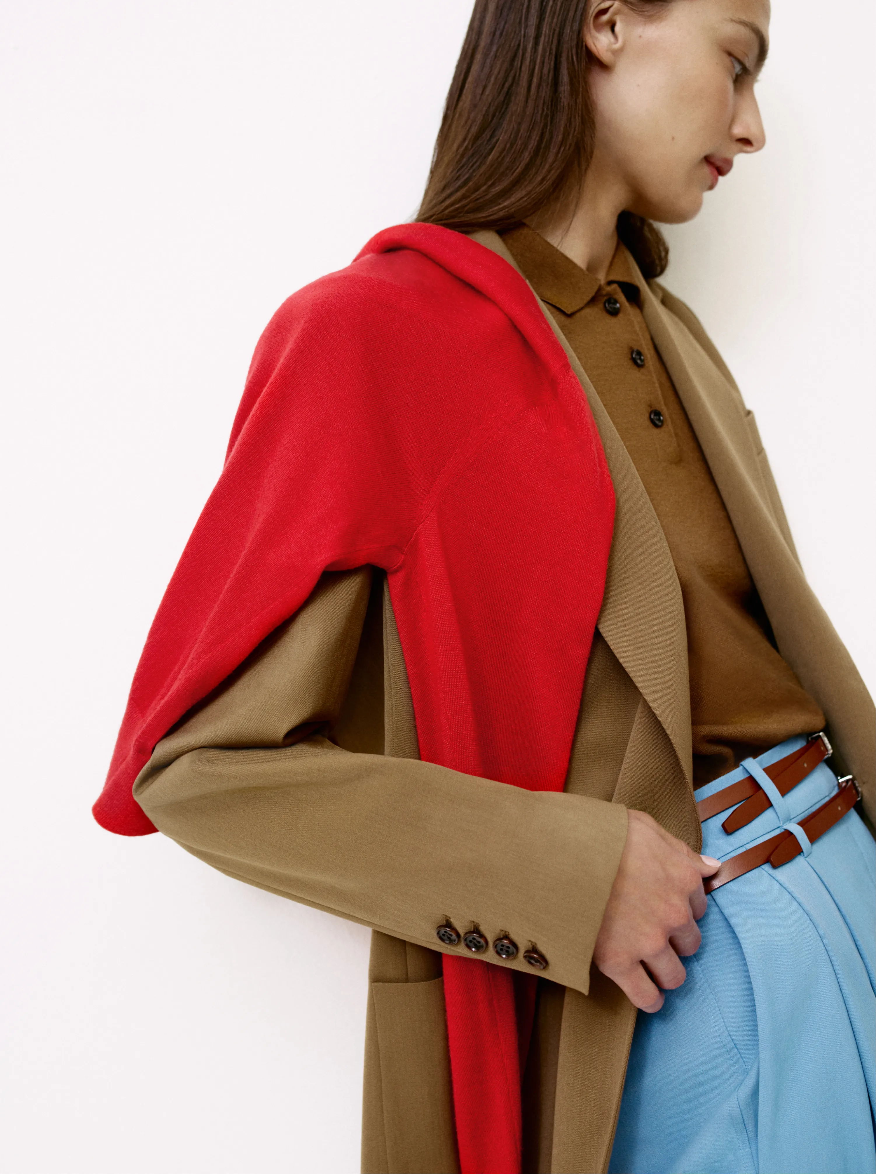 Woman in a brown shirt and red outerwear, wearing blue pants.