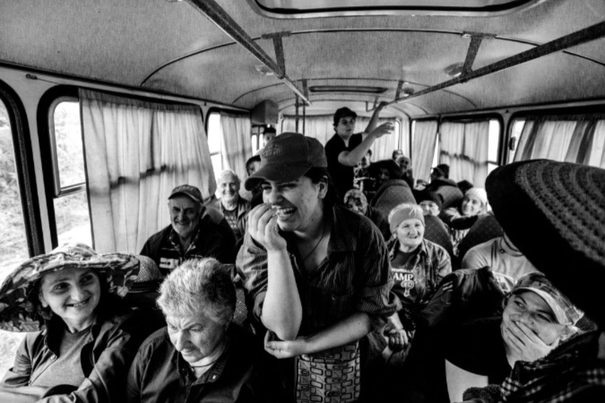 Black and white photo of people inside a bus, some laughing and interacting.