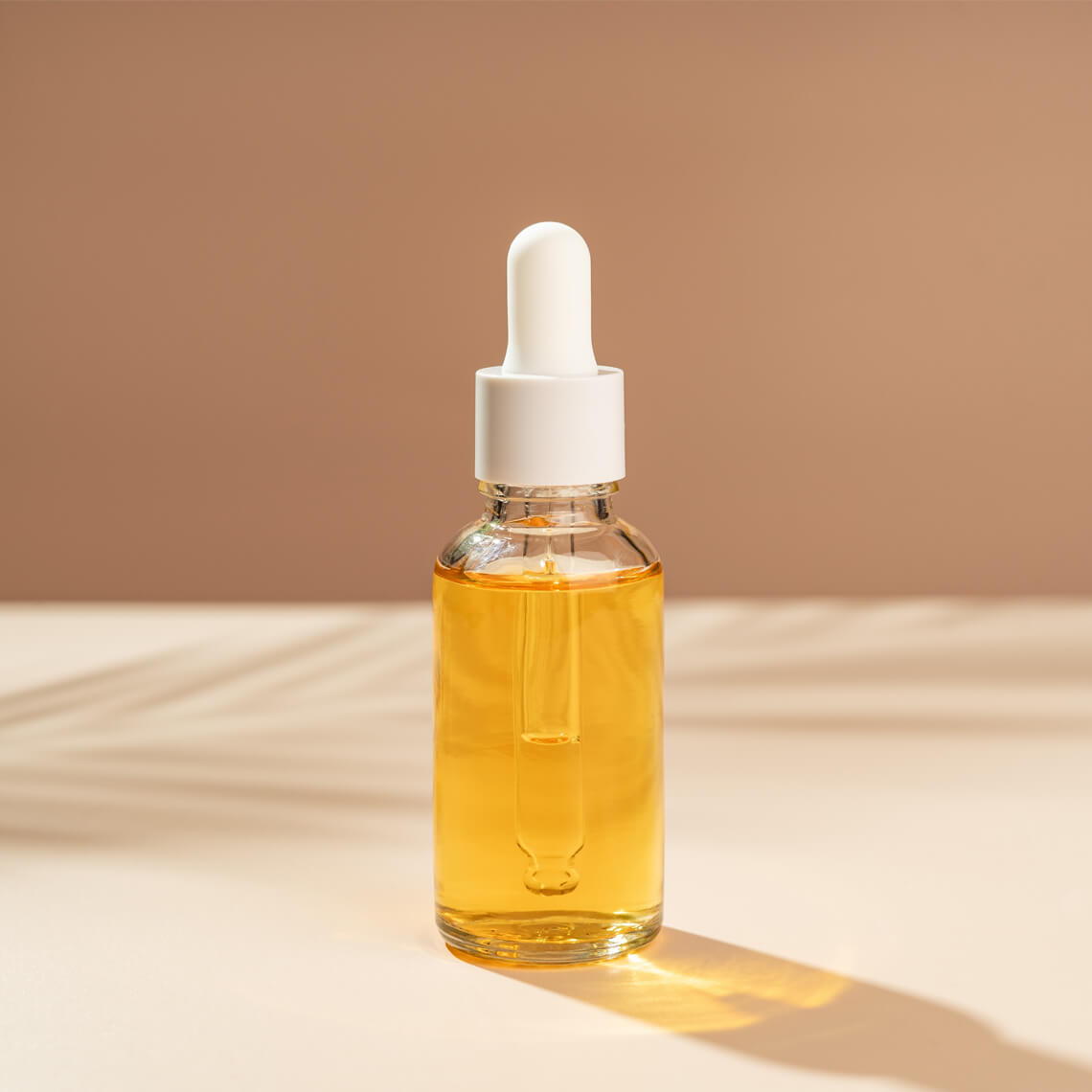 A glass dropper bottle filled with yellow oil on a light surface.