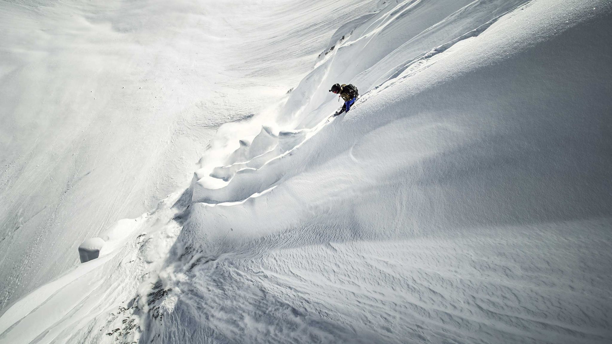 A snowboarder navigating a snowy mountain freeride.
