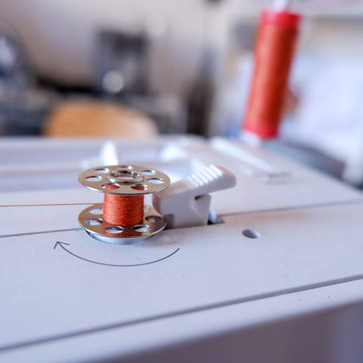 n bobbin being wound on a bobbin winder pin of a sewing machine with orange thread